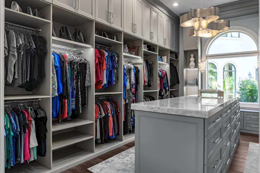 Photo of a women's closet with lots of hanging clothes and a island table top in the center