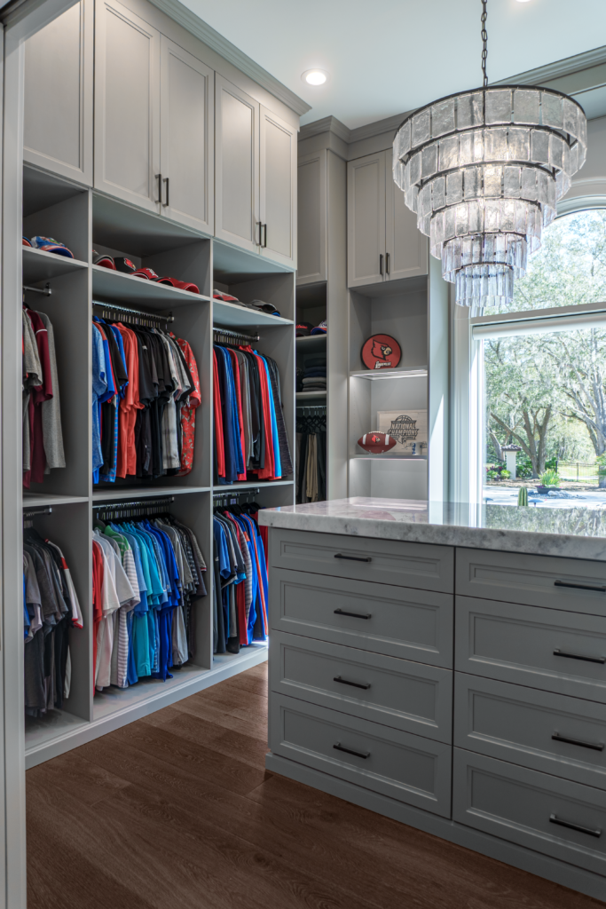 Photo of a men's closet with lots of hanging clothes and a island table top in the center