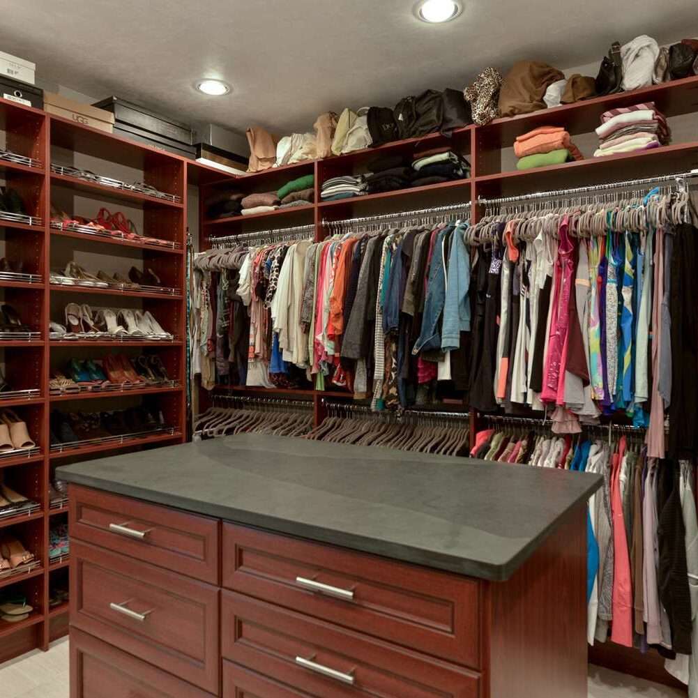 photo of a master closet filled with clothes and an island that has drawers